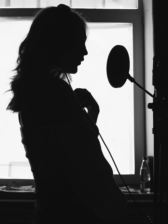 A dramatic silhouette of a woman singing into a microphone in a recording studio.
